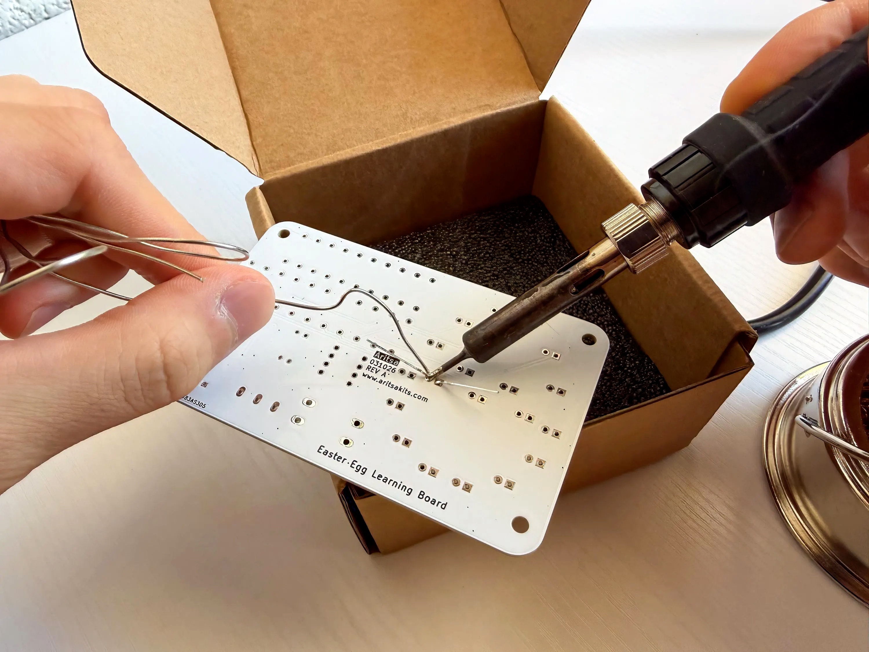Close-up of hands soldering the Easter Egg PCB with the iron in frame